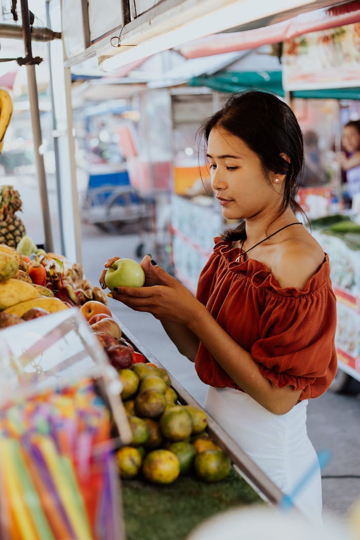 Young woman shopping for fresh fruits at an outdoor market, holding a green apple.